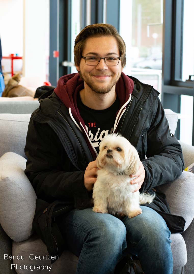 A student sat on a sofa with a white dog in their lap