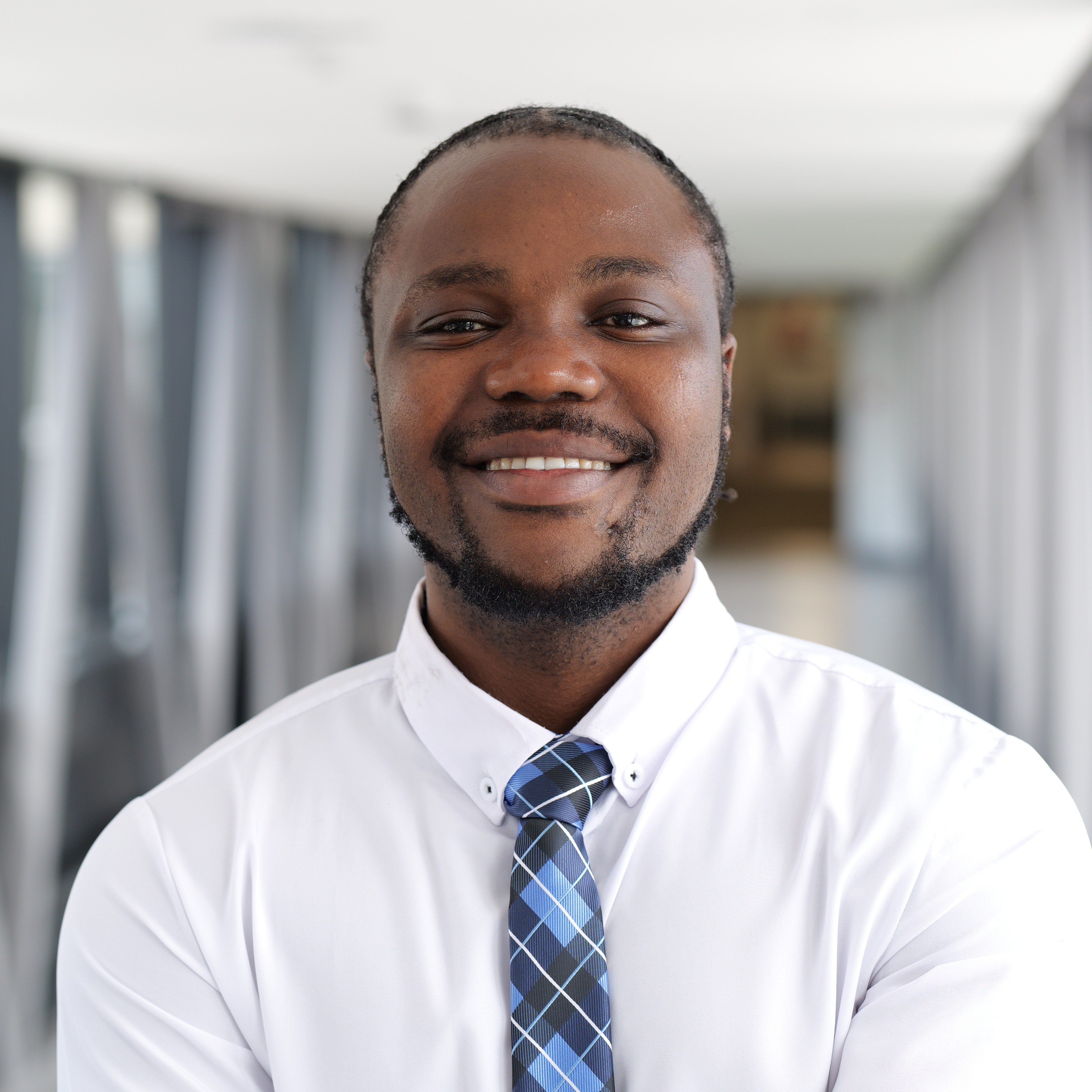 Photo of a black man (Student President) smiling in a white suit and blue tartan tie.