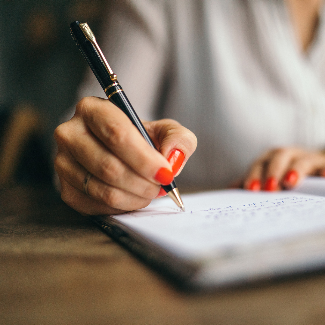 A hand with red nails writing with a pen